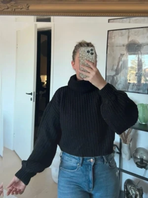 Kort Svart stickad polotröja - Snygg svart stickad polotröja. Tröjan har en hög krage som ger en trendig look. Perfekt att styla med jeans eller kjol för en cool vardagsstil.