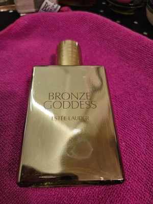 Bronze Goddess parfym från Estée Lauder - Lyxig parfymflaska i guldigt material från Estée Lauder, modell Bronze Goddess. Flaskan är fyrkantig med rundad guldfärgad kork och elegant design. Perfekt för dig som gillar exklusiva och somriga dofter.Mycket gott skick Använd någon enstaka gång Sälier parfvm från Estée Lauder Bronze Goddess Fau Fraiche Skinscent EDT 100ml En sensuell. soldränkt blandning av bergamott, varm am- ber, tiareblomma och vanili i kombination med utsökt krä- mig kokosnöt.