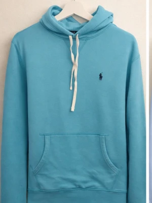 hoodie från Polo Ralph Lauren - Snygg ljusblå hoodie från Polo Ralph Lauren med vit dragsko och klassisk känguruficka. Liten mörkblå logga broderad på bröstet. Tillverkad i mjuk bomullsblandning och har huva för extra chill vibe.