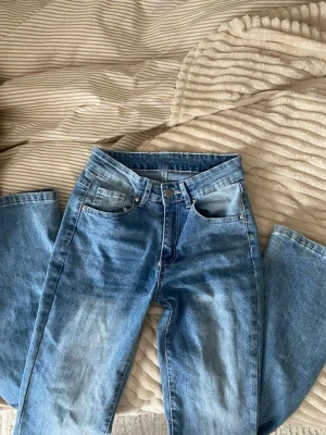 Blå bootcut jeans med broderad ficka - Säljer ett par ljusblå bootcut jeans med snygg broderad bakficka och knappdetalj. Jeansen har klassisk femficksmodell och är tillverkade i denim med lätt tvättad look. Perfekta för dig som gillar en avslappnad men trendig stil. Osäker på storlek men känns som xs
