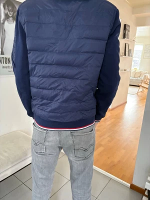 Mörkblå cardigan Ralph lauren  - Snygg mörkblå cardigan från Ralph lauren och släta ärmar. Jackan har ribbade muddar med röd, vit och marinblå rand vid midjan. Praktisk ficka på ärmen och sportig look. Perfekt för dig som vill ha en stilren och modern jacka.