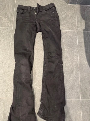 Svarta True religon jeans - Säljer ett par svarta bootcut jeans med låg midja och klassisk femficksmodell. Jeansen har utsvängda ben. Storlek 24( rätt långa i benen) 