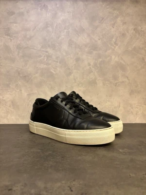 Axel Arigato Orbit Vintage - Snygga svarta sneakers från Axel Arigato i slätt skinn med vit, tjock sula. Klassisk låg modell med rund tå och svarta snören. Minimalistisk design med diskret logga på sidan. Perfekta till jeans eller chinos för en clean look. I bra skick!