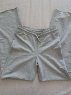 Grå mjukisbyxor med snörning - Gråa mjukisbyxor i klassisk modell med resår och snörning i midjan. Byxorna har raka ben och är tillverkade i mjukt material, perfekta för en avslappnad stil. Passar dig som gillar enkel och bekväm design. Har sprättat upp byxorna där nere för att göra de "lite längre" eftersom de var för korta för mig.