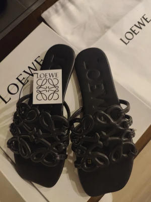 Svarta sandaler från Loewe - Snygga svarta sandaler från Loewe med unik flätad design på ovandelen. Tillverkade i läder med fyrkantig tå och låg sula. Perfekta för dig som vill ha något trendigt och exklusivt till sommaren. Ikonisk Loewe-logga på innersulan.