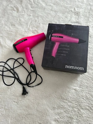 Rosa hårfön från nomnom - Säljer en rosa hårfön från nomnom, modell Fairy Tale. Hårfönen har svart handtag och detaljer, samt flera värme- och hastighetsinställningar. Kommer med originalkartong. Perfekt för dig som vill ha en snygg och praktisk hårtork.