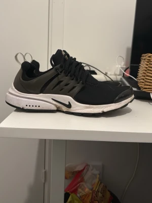 Nike Presto - Säljer ett par svarta Nike Air Presto sneakers med vit sula och svart swoosh. Skorna har en mesh-överdel, plastdetaljer på sidorna och elastiska snören. Perfekta för dig som gillar sportig och clean stil. Skorna är i jätte bra skick fast behöver bara tvättas o de gör jag såklart innan jag fraktar dom.