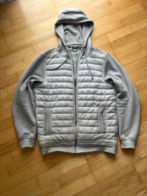 Grå hoodie-cardigan från Livergy - Snygg grå hoodie-cardigan från Livergy med quiltad front och mjuka ärmar i sweatshirtmaterial. Jackan har dragkedja, två fickor fram och en skön huva med dragsko. Perfekt för lager-på-lager och chill stil.