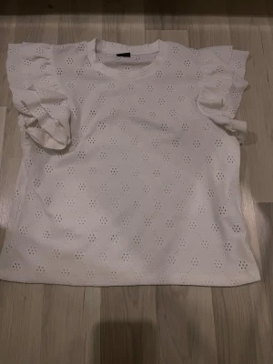 Vit blus med volangärmar från Gina Tricot - Supersöt vit blus från Gina Tricot med broderade hålmönster och volangiga korta ärmar. Storlek s🩷