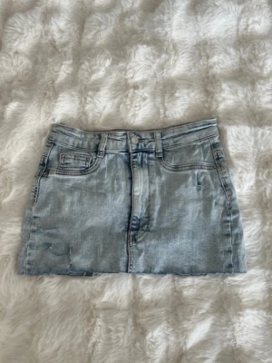 Ljusblå jeanskjol från Gina Tricot - Säljer en snygg ljusblå jeanskjol från Gina Tricot, modell Molly. Kjolen har en knapp och dragkedja framtill samt en rak, kort passform. 