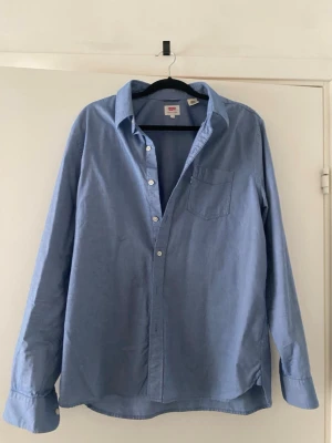 Blå skjorta från Levi's i bomull - Klassisk blå skjorta från Levi's i mjuk bomull. Skjortan har lång ärm, bröstficka och knappar framtill. Perfekt oversized look och enkel att styla till olika outfits.