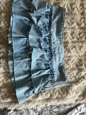 Ljusblå volangkjol i denim - Supersöt kort kjol i ljusblå denim med volangdetaljer och råa kanter. Kjolen har en bred linning och ger en avslappnad men trendig look. Perfekt att matcha med en enkel topp för en cool outfit.