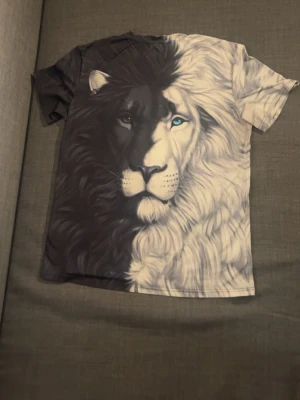 T-shirt med lejonmotiv i svart och vitt - Cool t-shirt med stort tryck av ett lejon i svart och vitt som täcker hela framsidan. Ena halvan av lejonet är svart med mörka detaljer, andra halvan är vit med blått öga. Perfekt statement-plagg för dig som gillar unika motiv.