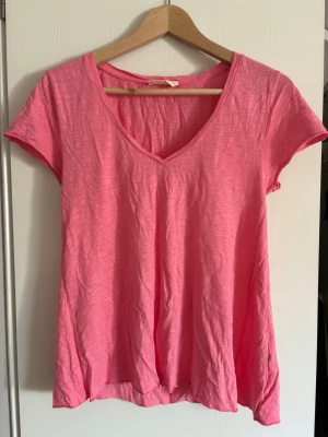 Rosa v-ringad t-shirt American Vintage - Snygg rosa t-shirt från American Vintage med v-ringning och korta ärmar. T-shirten har en avslappnad passform och är tillverkad i mjuk bomull, perfekt för en chill och stilren look.