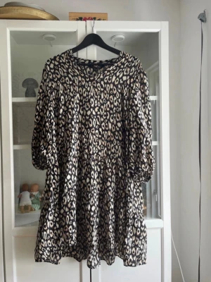 Leopardmönstrad klänning KappAhl M - Snygg kort klänning från KappAhl med leopardmönster i svart och beige. Klänningen har trekvartsärmar och en lös passform som ger en avslappnad vibe. Perfekt för dig som gillar djurmönster och vill sticka ut lite extra.