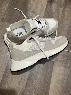 Vita Skor med monogram - Snygga vita sneakers med ikoniskt monogrammönster på sidan, detaljer i mocka och mesh samt svarta detaljer vid snörningen. Skorna har en chunky vit sula med svart undersida och klassisk låg profil. Perfekta för dig som vill sticka ut med lyxig streetstyle. Helt ny.