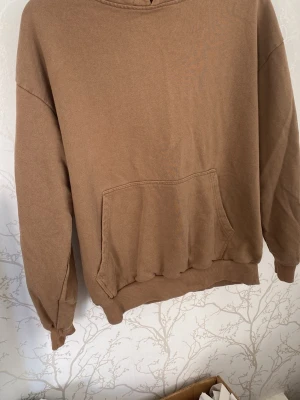 Beige oversized hoodie med ficka - Säljer en beige oversized hoodie med stor känguruficka framtill och ribbade muddar vid ärmslut och nederkant. Hoodien har en klassisk huva med metallöljetter för snören (snören saknas). Perfekt för en chill och avslappnad stil.
