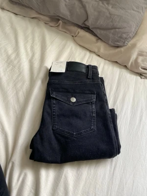 Svarta bootcut jeans från Vailent - Svarta bootcut jeans från Vailent med medelhög midja och smal passform över låren. Jeansen har en snygg ficka med lock och knapp bak samt klassisk femficksdesign. Helt nya med lappar kvar, endast testade. Pruta om så behövs för jag vill bara bli av med de🤠🥰