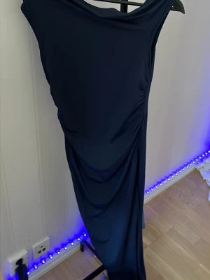 Långklänning i marinblått och vinrött - Två eleganta långklänningar i marinblått och vinrött med draperad effekt längs sidan. Klänningarna har en smickrande, åtsittande passform och är ärmlösa. Perfekta för dig som vill sticka ut med stilren look.