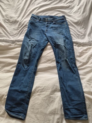 Blå raka jeans från diesel  - Säljer ett par klassiska blå jeans från Levi's med rak passform och normal midja. Jeansen har fem fickor, knappgylf och snygga slitningar framtill för en avslappnad look. Perfekta till vardagsstilen och tillverkade i slitstarkt denimtyg.