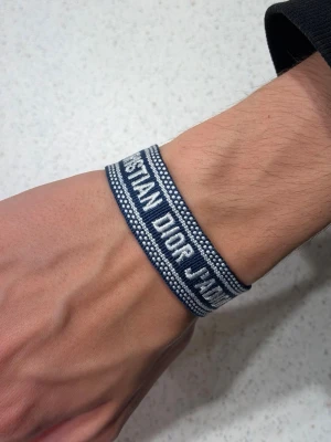 Blått armband  - Snyggt vävt armband med text på. Armbandet har justerbar knytning och fransar i ändarna. Perfekt accessoar för att lyfta din outfit med en lyxig touch.