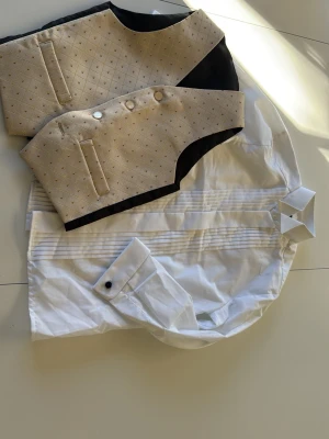 Jackett nyskick kostym med beige väst stl 120 - Perfekt för den lille gentlemannen att klä upp sig i skjorta, väst, byxa och långkavaj. Allt endast provat eldrig användt. Snygg kostym med svart kavaj, randiga grå byxor och en beige väst med diskret mönster och knappar. Vit skjorta med veckad front ingår. Perfekt för dig som vill sticka ut med klassiska detaljer och modern touch.