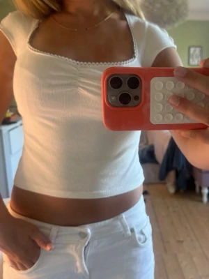 Vit ribbad croppad topp - Säljer en vit ribbad croppad topp med korta ärmar och söt spetskant vid den fyrkantiga urringningen. Toppen har en lätt rynkning framtill och är perfekt för dig som gillar en enkel men ändå detaljerad stil.