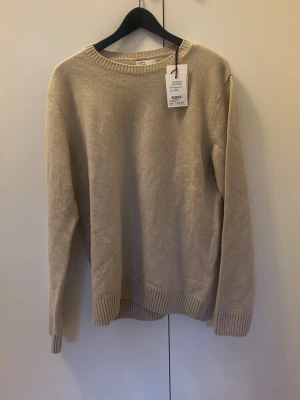 Beige merinoulltröja Colorful Standard - Snygg beige stickad tröja från Colorful Standard i mjuk merinoull. Klassisk rund halsringning och ribbade muddar vid ärmslut och nederkant. Perfekt för lager på lager och enkel att matcha med olika outfits.