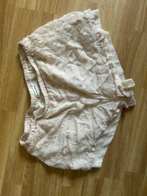 Ljusrosa pyjamasshorts med spets  - Säljer ett par ljusrosa shorts från Pull and Bear med fina spetsdetaljer och diskret blommönster. Shortsen har elastisk midja och är tillverkade i ett mjukt, tunt material som passar perfekt till varma dagar.