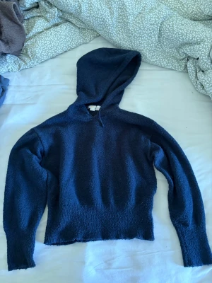 Mörkblå stickad hoodie - Mysig mörkblå stickad hoodie med lång ärm och avslappnad passform. Tröjan har en stor huva och är tillverkad i ett mjukt, fluffigt material som känns skönt mot huden. Perfekt för dig som gillar en enkel men stilren look.