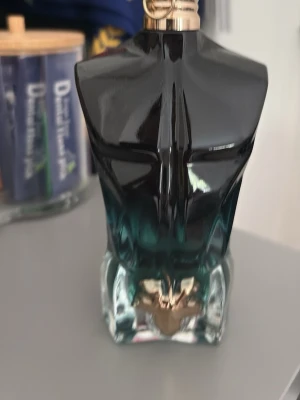 Le Male parfymflaska från Jean Paul Gaultier - Unik parfymflaska formad som en manlig torso i svart och turkost glas med metallisk detalj vid basen. Flaskan har en modern och konstnärlig design som verkligen sticker ut i badrumshyllan.
