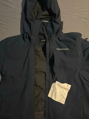  Peak Performance Hipe core jacka - Peak Performance Hipe core jacka. Se annons sista bild. En riktigt bra varm jacka till när man åker skidor. Otroligt många fickor utanpå och innanför jackan. Även puts duk för skidglasögon i fram fickan på bröstet. Jackan har även ventilations fickor på ryckens höger och vänster sida ifall de blir för varmt. Jackan är i nyskick då den bara använts en vinter.