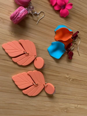 Färgglada statement örhängen i polymerlera - Säljer ett set med unika örhängen macaron örhängena är gjorda  i polymerlera: ett par i form av orange blad, ett par med vågiga blå och orange former,  och ett par rosa blommor. Perfekta för dig som gillar färg och lekfull design.