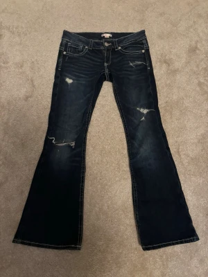 Mörkblå bootcut jeans med slitningar - Säljer ett par mörkblå bootcut jeans med snygga slitningar och kontrastsömmar. Jeansen har låg midja och klassisk femficksmodell. Perfekta för en avslappnad och trendig look. Storlek 164+ men passar xs-m. 🫶🏻