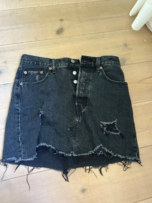 Svart Levis jeanskjol - Svart Levis jeanskjol med små slitningar! Den är i bra skick! Motsvarar storlek xs-s kanske