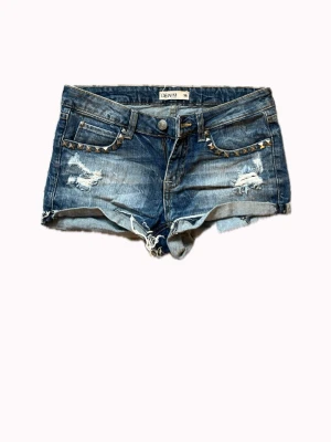 Blå denimshorts med nitar - Snygga blå jeansshorts från Denim med slitna detaljer och coola nitar längs fickorna. Perfekta för varma dagar och ger en edgy streetstyle-look. Storlek 36