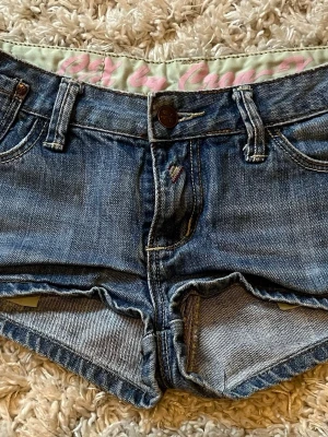 Blå jeansshorts från Juicy Couture - Säljer ett par klassiska blå jeansshorts från Juicy Couture. De har låg midja, råa kanter och femficksmodell. Shortsen är i denim med knapp och dragkedja framtill samt bälteshällor. Perfekta för sommaren! Säljer pågrund av att jag inte använder shorts så ofta! Jag är 34/36 och de sitter perfekt på mig! Säljer för 200 men priset kan diskuteras! 