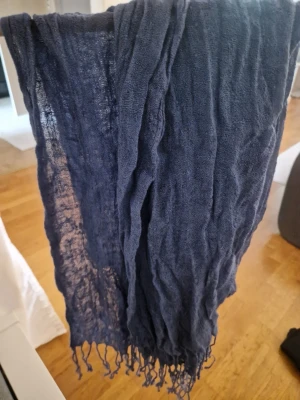 Mörkblå tunn sjal med fransar - En snygg mörkblå sjal i tunt, luftigt material med fransar i kanterna. Perfekt att slänga över axlarna för en avslappnad look. Sjalen har en lätt skrynklig struktur som ger en cool vibe.