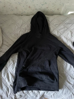 Svart hoodie från H&M - En klassisk svart hoodie från H&M med stor huva och magficka. Hoodien har ribbade muddar vid ärmslut och nederkant. Perfekt för en avslappnad och stilren look. Tillverkad i mjukt bomullsmaterial som känns skönt mot huden. Bra passform!