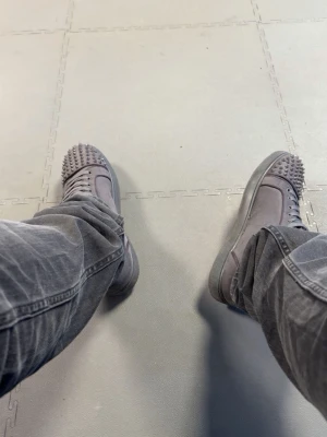 Christian Louboutin svarta spikes sneakers - Säljer ett par svarta sneakers från Christian Louboutin med ikoniska röda sulor och coola spikes på tån. Skorna har en klassisk låg modell med snörning och är tillverkade i mocka. Perfekta för dig som vill sticka ut med din stil.