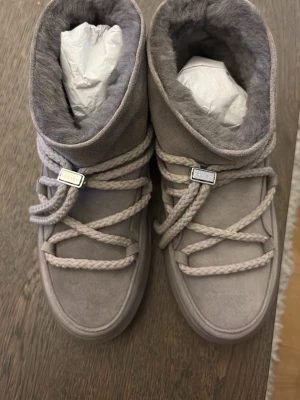 Gråa Inuikii classic low - KOSTADE 2500 KR! HELT NYA OCH KOMMER I ORGINAL FÖRPACKNING! SÄLJER EFTERSOM DE INTE PASSADE! Säljer ett par gråa Inuikii i mjuk mocka med fluffigt foder och grova snören. Skorna har en chunky sula och högt skaft som ger en riktigt cozy vinterlook. Perfekta för dig som vill ha både stil och värme under kalla dagar. SÄLJER ENDAST I 1-3 DAGAR SÅ PASSA PÅ! ANNARS LÄMNAR JAG TBX DEM