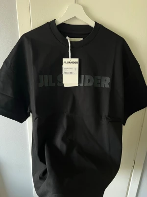 Svart J. Sander t-shirt i bomull - Svart t-shirt från Jil Sander med diskret logga tryckt framtill. Klassisk rund halsringning och korta ärmar. Tillverkad i mjuk bomull för en skön och stilren känsla. Perfekt för dig som gillar minimalistisk design.