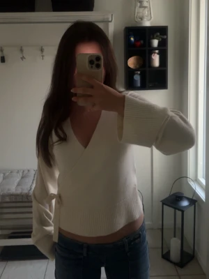 Vit omlottkofta med ribbade detaljer - Snygg vit omlottkofta med breda ärmar och ribbade muddar. Koftan har en knytning i sidan och djup v-ringning, perfekt för att skapa en avslappnad och trendig look. Materialet ser ut att vara mjukt och stickat.