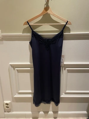 Svart spetsklänning slip dress | Minus | XS/34 | Ny - Säljer denna eleganta och feminina slipklänning från det danska märket Minus. Klänningen har spetsdetaljer vid urringningen och nederkanten, justerbara spaghettiband och en mjuk satinskimrande känsla. Perfekt som aftonklänning eller till festliga tillfällen. Märke: Minus Modell: Asa Slipover Dress Färg: Black Iris (mörkblå/marinblå) Material: 92% Polyester Storlek: XS Skick: Helt ny med lappar kvar Ordinarie pris: 850 kr Längd: 86 cm Axelbredd: 30 cm Frakt tillkommer. 