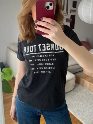 Svart t-shirt med tryck - Säljer en mörkgrå t-shirt med vit tryck i fram. T-shirten har rund hals och korta ärmar, perfekt till jeans eller shorts. Skön och enkel stil som funkar till det mesta.