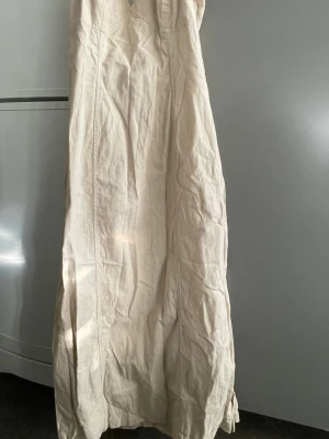 Beige halterneck klänning i bomull/linne - Snygg och enkel långklänning i beige bomull/linne. Stretchig med slits på bägge sidor. Dragkedja bak.. Stilren design utan mönster eller extra detaljer, vilket gör den lätt att matcha med accessoarer. Nu är den ostruken pga att den legat nerpackad men jättesnygg.  Endast använd en el två ggr.