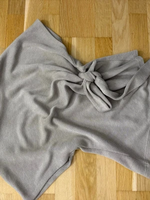 Ljusgrå stickad halsduk - En mjuk och stilren ljusgrå halsduk i stickat material. Halsduken har en enkel design med slätstickad yta och kan knytas på flera olika sätt för en personlig look. Perfekt accessoar för att lyfta din outfit.