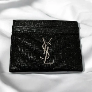 Svart kortfod sop från Saint Laurent - Snygg svart kortfodral i präglat läder från Saint Laurent med ikoniska YSL-loggan i silver framtill. Fodralet har flera kortfack och en stilren, minimalistisk design som passar perfekt i fickan.