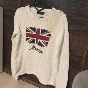 Vit stickad tröja Morris Lady - Vit stickad tröja från Morris Lady med Union Jack-flagga i rött, blått och vitt på bröstet samt broderad Morris-text under. Tröjan har rund halsringning och ribbstickade muddar. Perfekt för dig som gillar klassisk brittisk stil. Köpt begagnat för cirka 900kr men använde aldrig den då jag ångrade köpet! Lite fläckig men inte så synligt. !LITEN I STORLEK! Jag har vanligtvis S, denna i M passar precis.