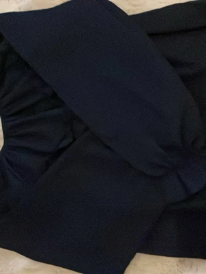 Mörkblå offshoulder blus - Trendig mörkblå offshoulder blus med långa puffärmar och smockdetaljer vid ärmslutet. Tillverkad i ett mjukt, vävt tyg som ger en snygg siluett. Perfekt att styla med både jeans och kjol för en cool look.